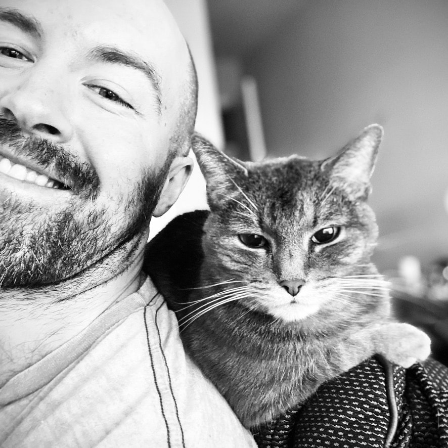 Black and white close-up of Julian Murphy smiling beside a cat